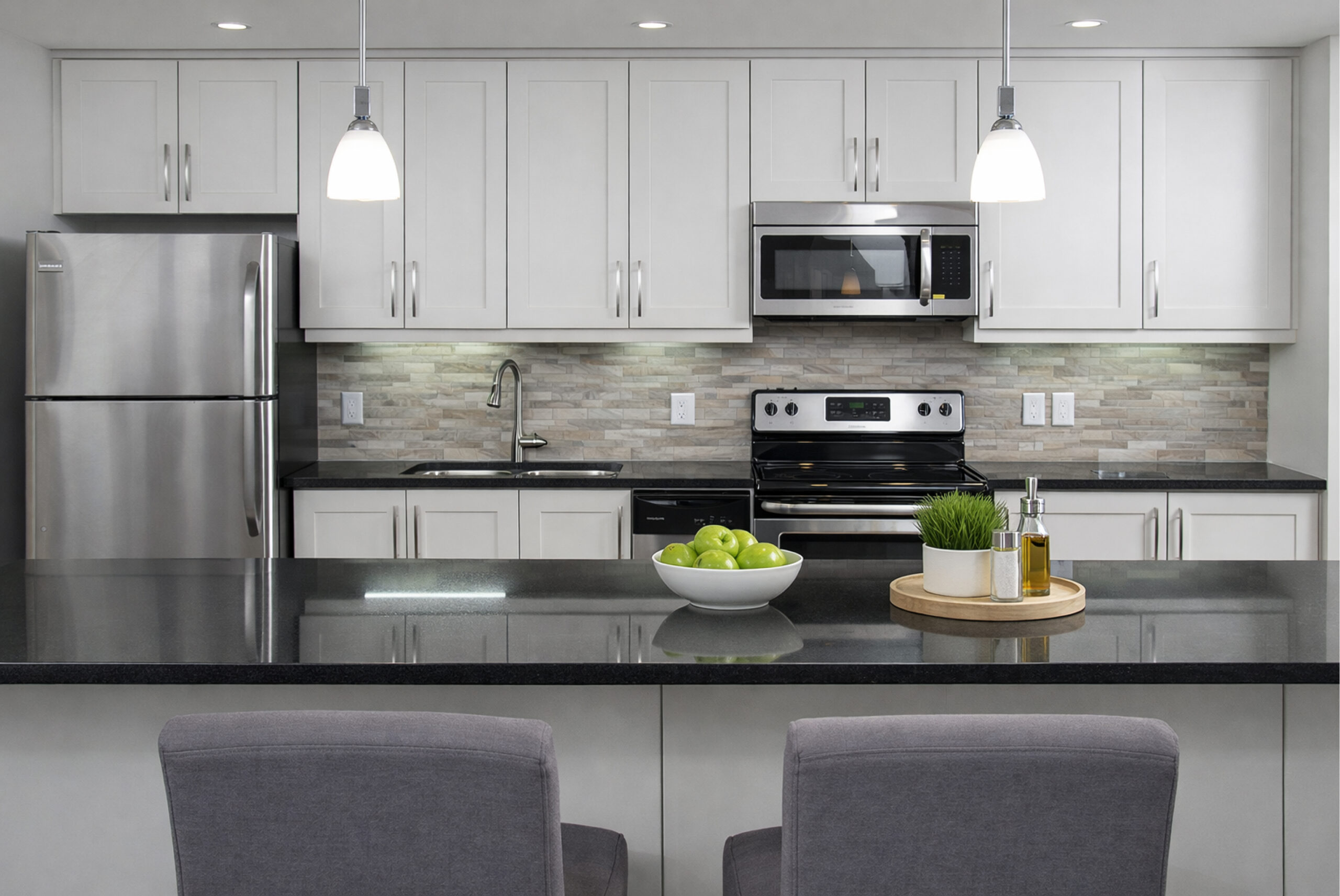 DeSantis condominium unit kitchen with black granite countertop, white cabinets and stainless appliances.