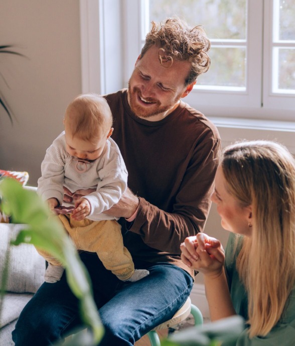 DeSantis Developments New Homes Hero Image of a Mother and Father holding their young baby in a bright, sunny room